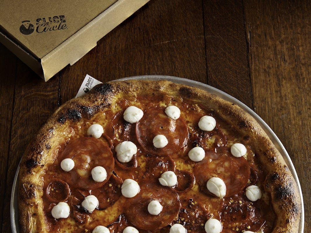 A Slice Circle pizza on a metal tray next to a Slice Circle takeaway box