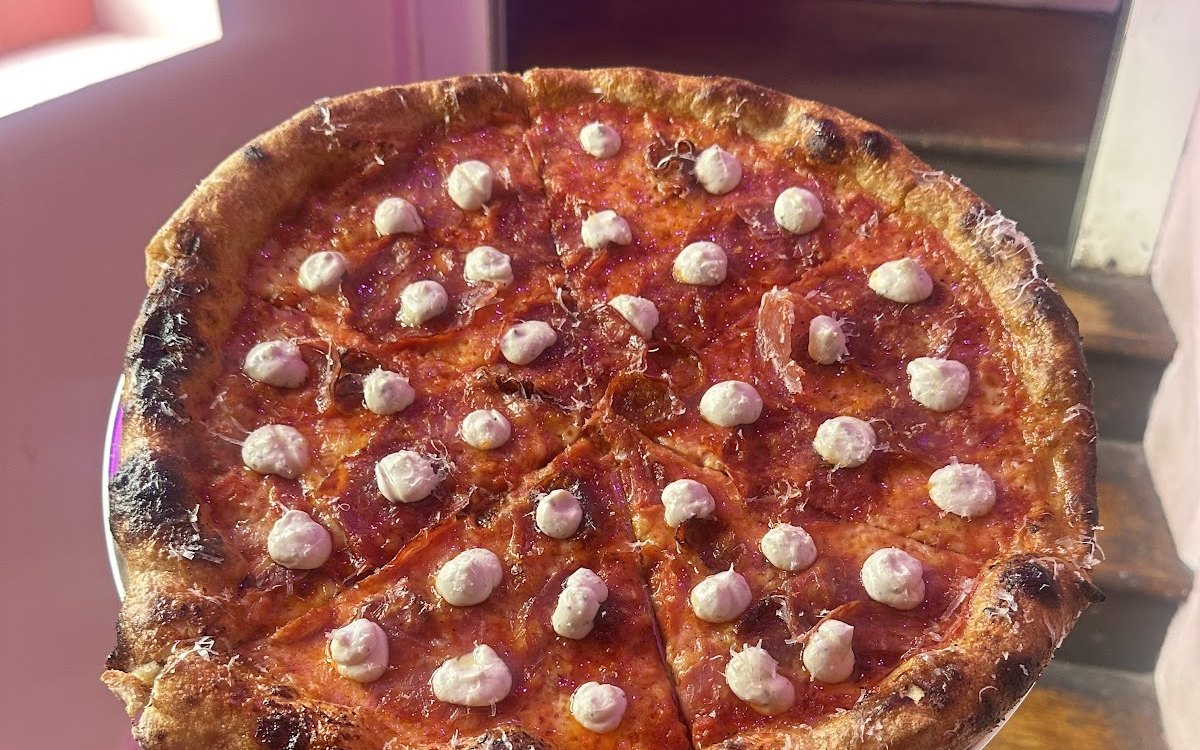 A whole Slice Circle pizza held up on a tray in a pink-lit room