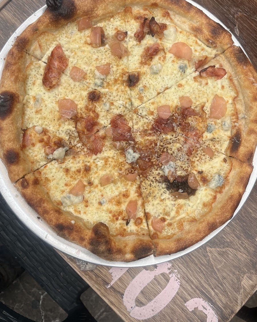 A pizza on a metal tray on a wooden table outside